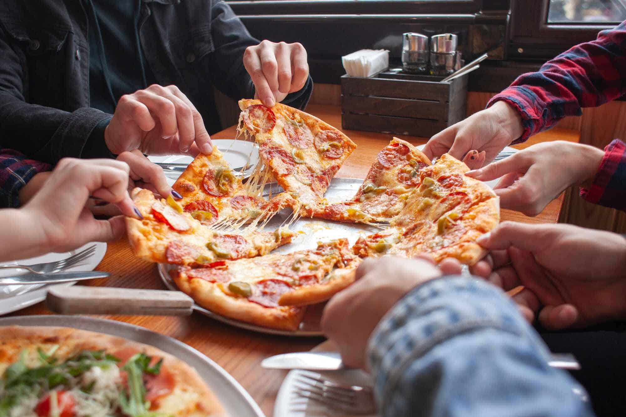 Friends sharing a large pizza at a cozy restaurant, hands reaching out to grab steaming hot slices with stringy cheese