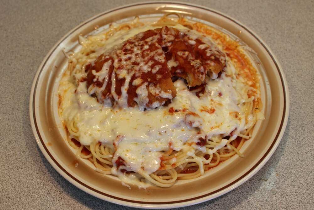 Crispy chicken Parmesan A plate of chicken Parmesan served on a bed of spaghetti, topped with melted mozzarella cheese and marinara sauce, with the breaded chicken cutlet slightly crisp and golden-brown, all on a beige plate set on a granite countertop.