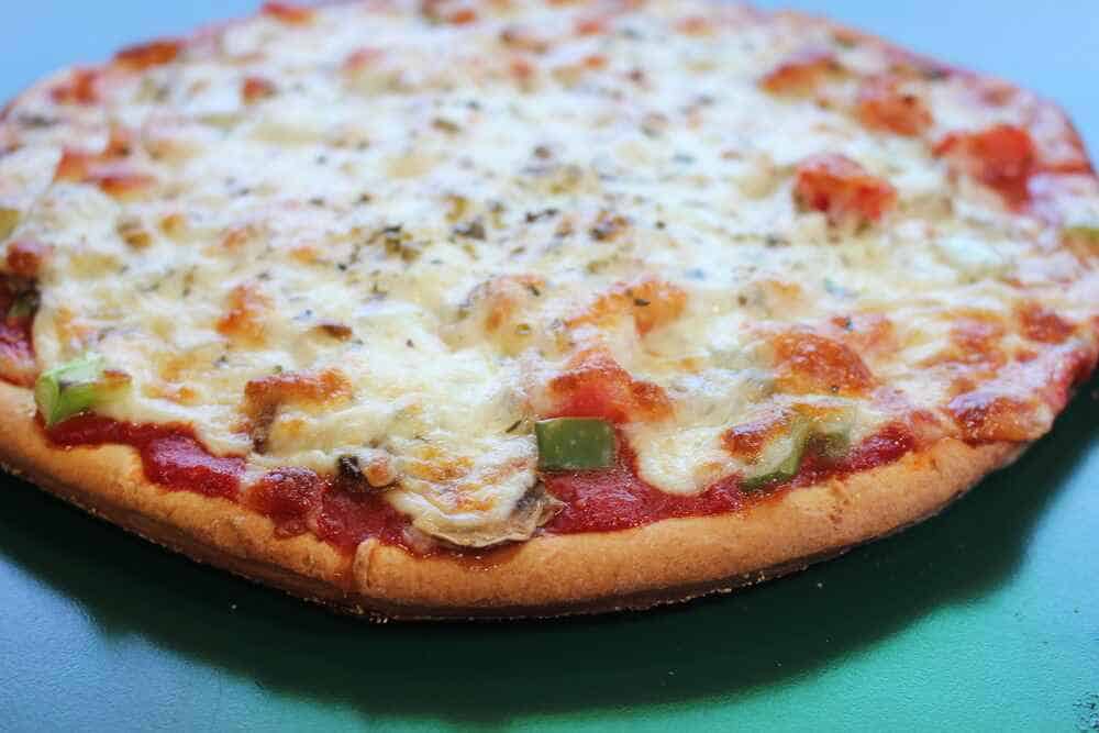 A freshly baked thin-crust pizza with melted mozzarella cheese, diced green bell peppers, and a sprinkle of Italian herbs on top, served on a teal table surface.